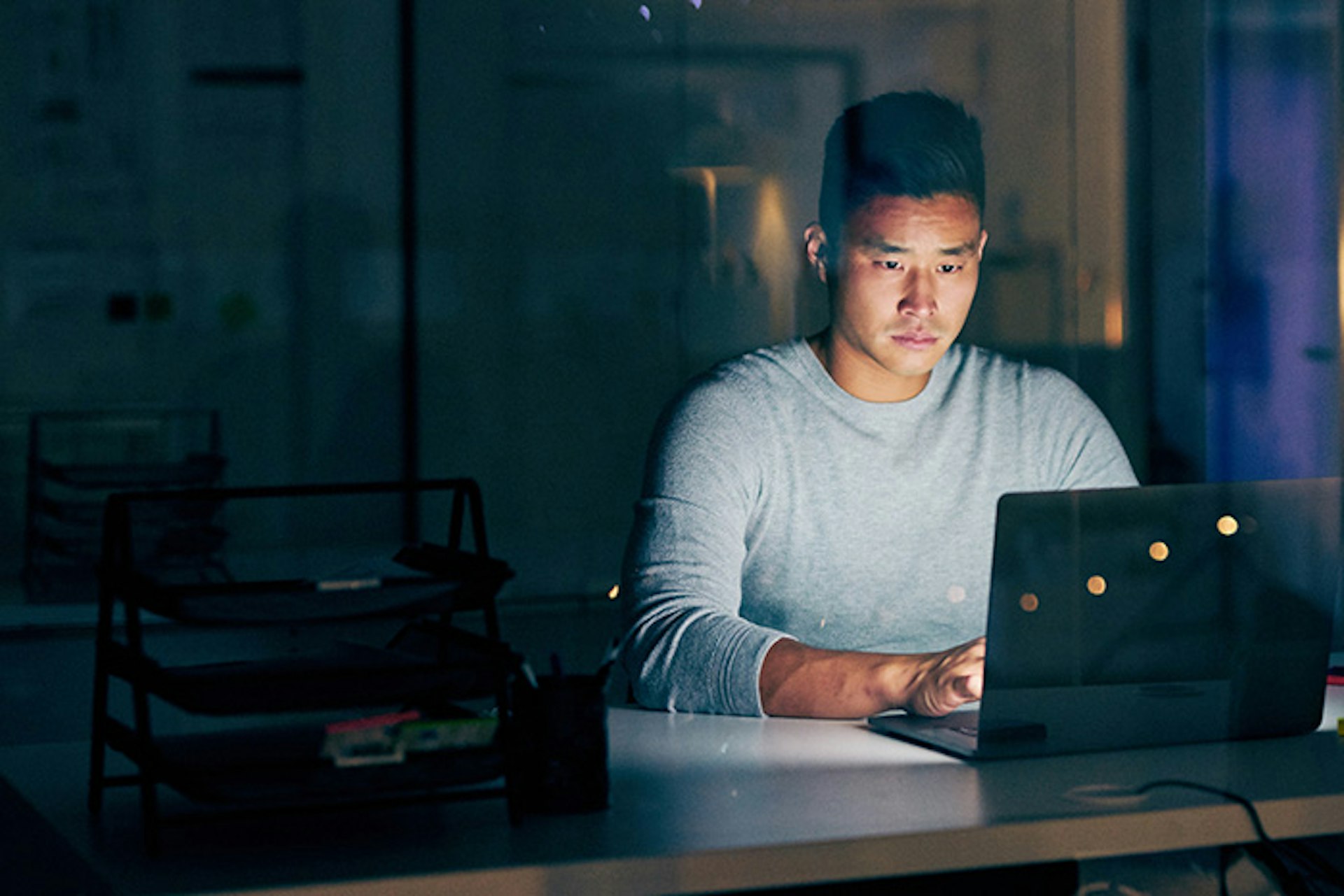 Homem iluminado por laptop em um quarto escuro