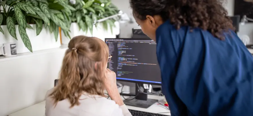 Mulheres olhando código de programação em um monitor